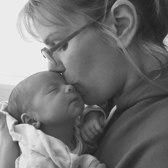 Mom holding newborn baby upright while kissing his face.