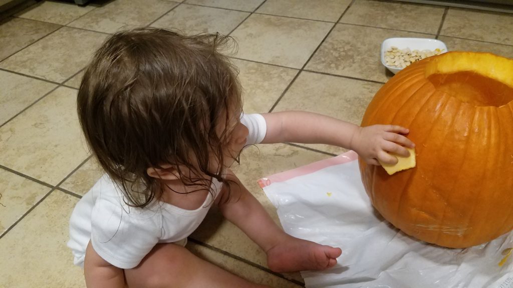 Mama Rissa's toddler putting carved eye pieces back into the pumpkin like a puzzle.