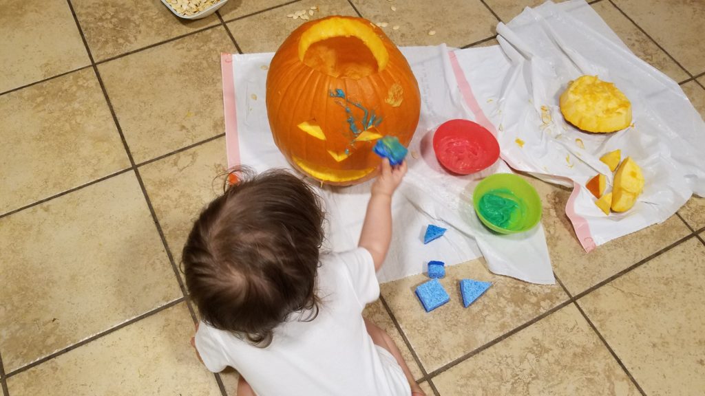 Mama Rissa's toddler applying paint to her carved pumpkin with a sponge.