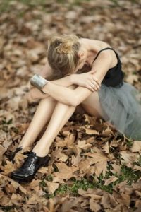 Woman sitting in leaves on the ground with her head in her arms trying to process miscarriage grief.