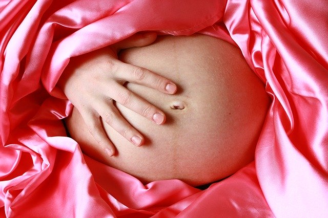 Pregnant belly surrounded by pink silk illustrating how pregnancy changes your body by reducing cancer risk. 