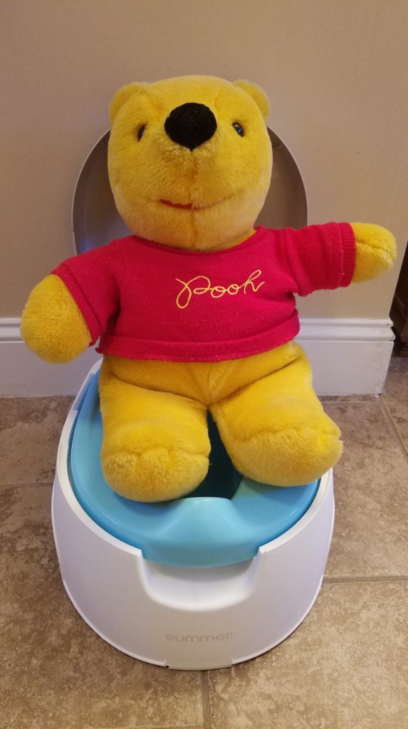 Stuffed Winnie the Pooh demonstrating sitting on a potty chair to prepare toddler for potty training. 