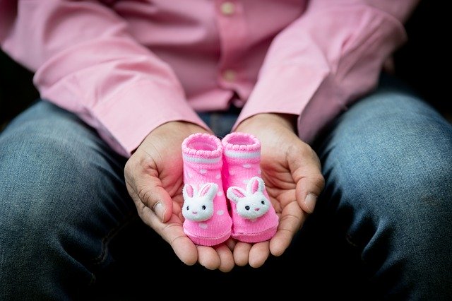 Dad holding pink baby shoes to announce having a baby girl.