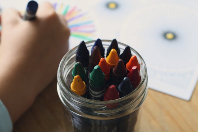Jar of crayons beside child coloring