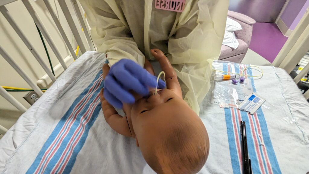 Nurse putting a baby feeding tube in a doll